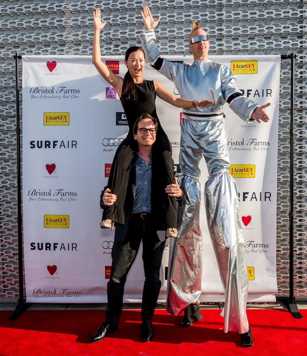 Dr. Jay Granzow, MD, holds his wife on his shoulders to match the height of a man in a silver suit and stilts at an event.